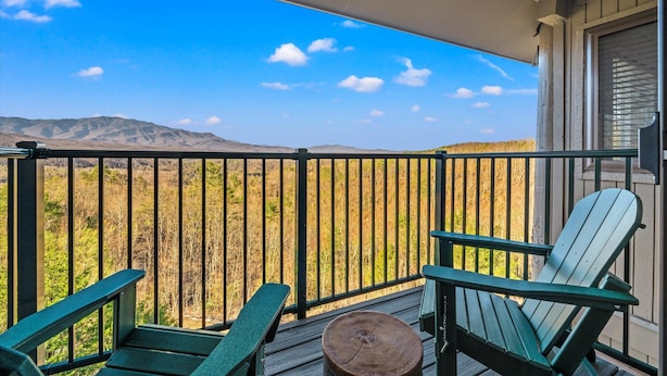 Un balcón con vistas a un paisaje desértico, dos sillas Adirondack y una mesa de madera.