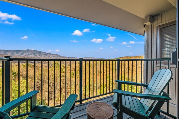 A balcony with a view of a desert landscape, two Adirondack chairs, and a wooden table.