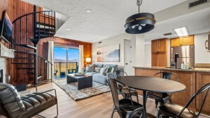 Un interior moderno con comedor, cocina y una escalera espiral que lleva a un balcón.