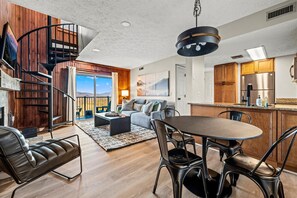 A modern interior with a dining area, kitchen, and a spiral staircase leading to a balcony.