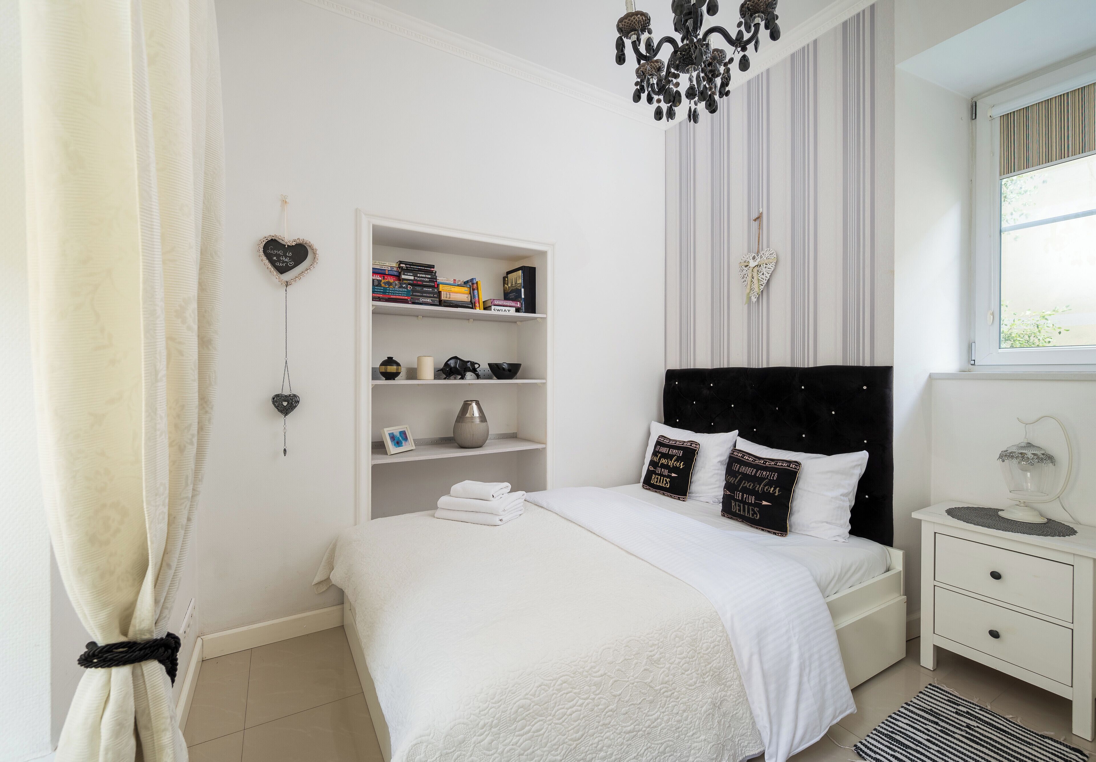 Una camera da letto ordinata con un letto, comodini, una libreria e una finestra con tende.