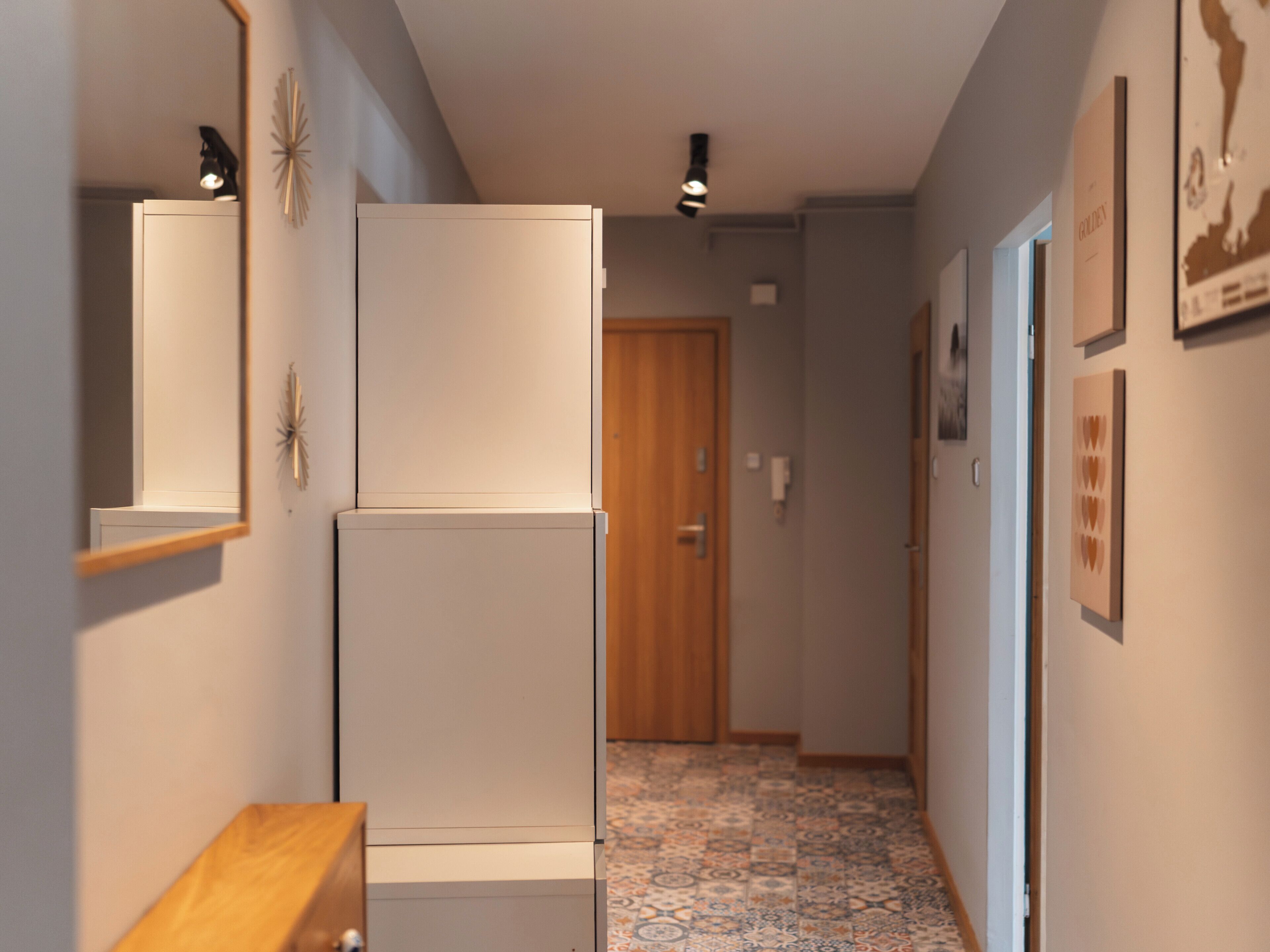 A narrow hallway with a white refrigerator, a wooden door at the end, and patterned floor tiles.