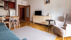 Ein kompakter Wohnbereich mit Küchenzeile, Essbereich, einer Sitzecke mit Sofa und Sesseln, einem kleinen Tisch und einem Fernseher auf einem Schrank.