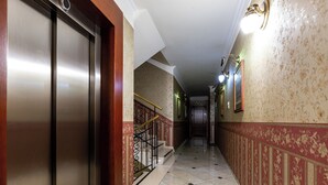 Ein Flur mit einer Metall-Glastür, einer Treppe mit wandförmigem rotem und goldenen Muster und einem gefliesten Boden.