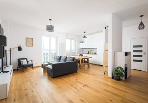 Relax in this spacious living area with a sofa set, dining table, and floor lamp, offering a view of the city outside.