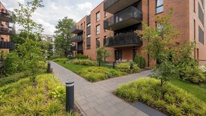 Un immeuble d’appartements moderne doté de balcons, d’une allée pavée et de jardins aménagés.