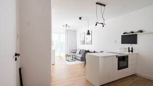 Une cuisine moderne avec des meubles blancs, un four encastré et un petit îlot central. On y trouve également un coin repas avec un canapé gris et une table basse.