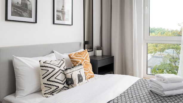 Une chambre d’hôtel bien rangée, avec un lit, des oreillers, une table de chevet et des tableaux encadrés accrochés au mur.