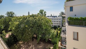 En bostadsbyggnad med en balkong, ett stort träd framför och ett avlägset torn i bakgrunden.