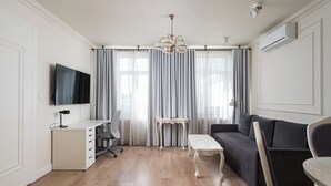 Ett modernt vardagsrum med trägolv, en grå soffa, ett vitt skrivbord med lådor, en vit stol och en tv som är monterad på väggen.