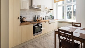 Una cocina moderna con armarios de madera, horno empotrado y zona de comedor con mesa y sillas.