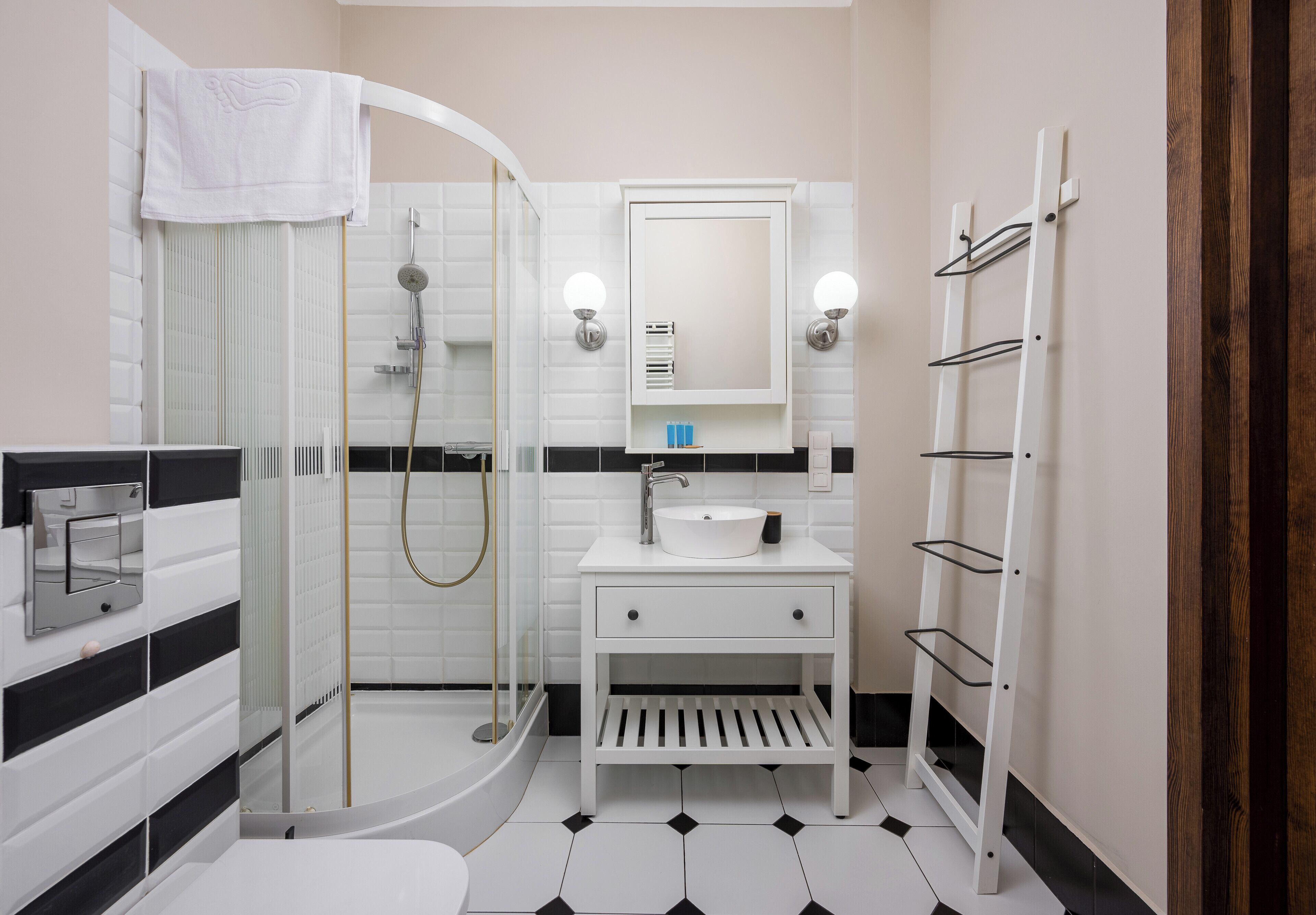 Un baño moderno con ducha de vidrio, un lavabo blanco con espejo y un perchero para toallas.