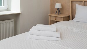 Una cama bien hecha con sábanas blancas y una toalla doblada al lado.