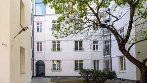 Un patio con un árbol, un sendero de ladrillo y un edificio blanco con varias ventanas y balcones.