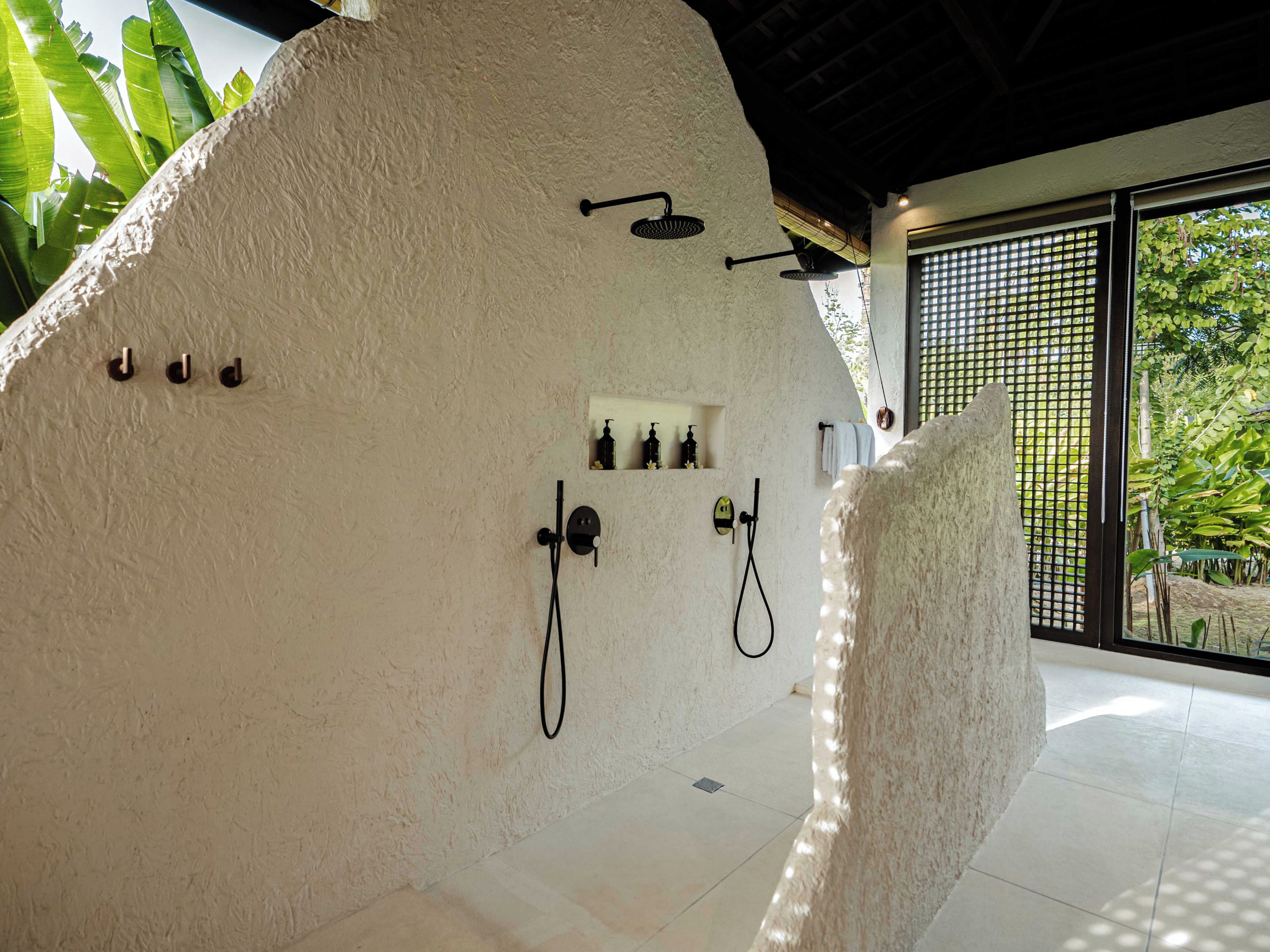Un bagno con una parete bianca a texture, una zona doccia e una finestra vista verde.