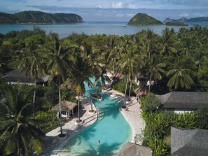 A resort with a swimming pool, palm trees, and a view of the sea. - Kuara Lombok - Adults Only Boutique Resort (Mertak)