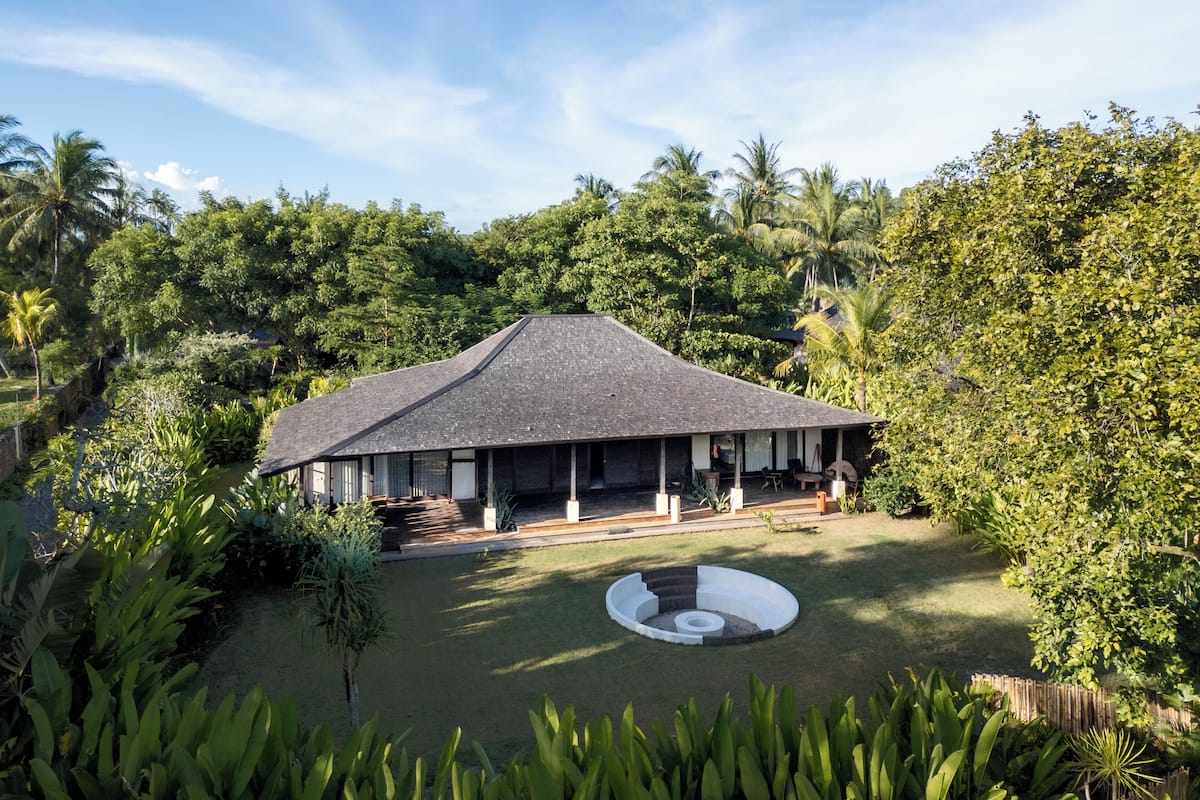 A modern house with a large deck, surrounded by lush greenery and palm trees.