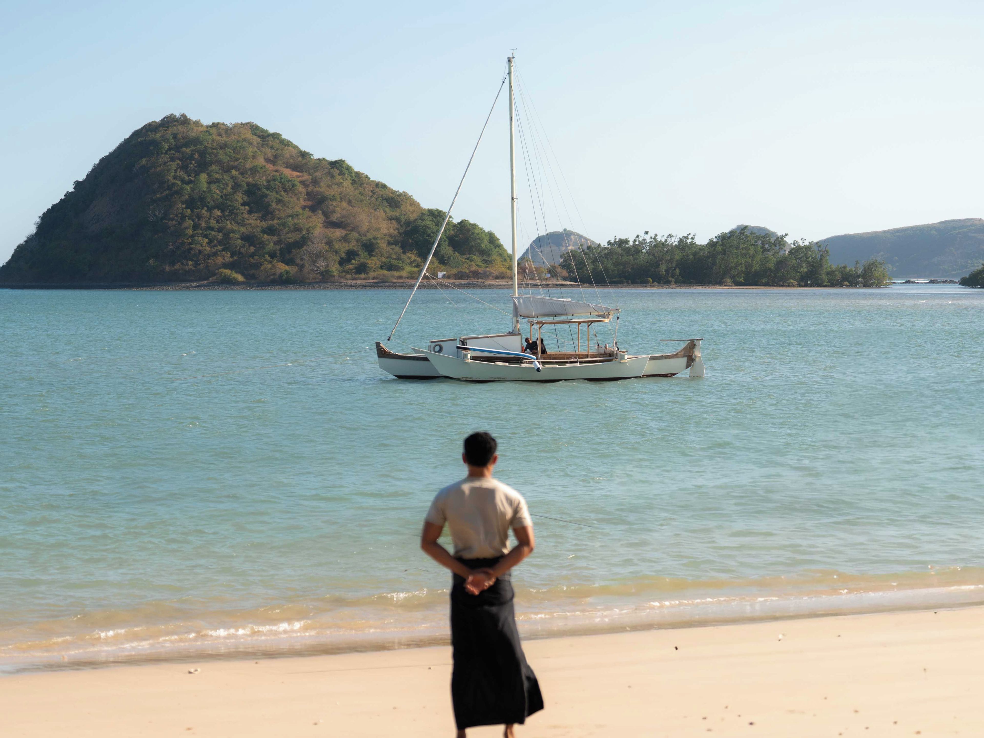 Uma praia com um barco na água e uma pessoa parada na costa.