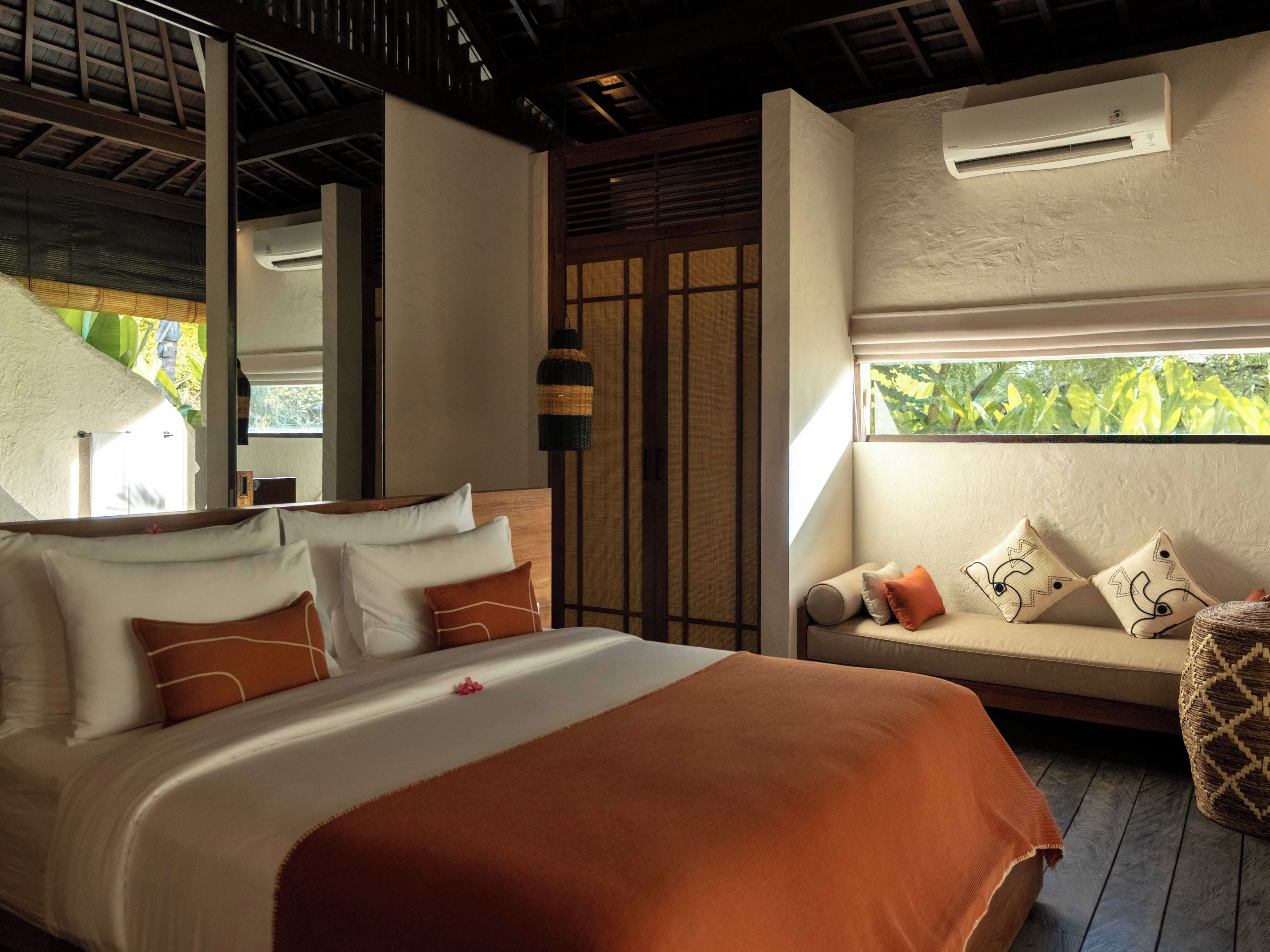A bedroom with a bed, a sofa, and a window with a view of greenery.