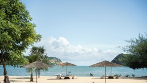 A beach with thatched umbrellas, a sandy beach, and calm water. - Kuara Lombok (Mertak)