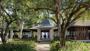 A covered pathway leading to a gazebo-like structure surrounded by lush greenery and trees. - Kuara Lombok (Mertak)