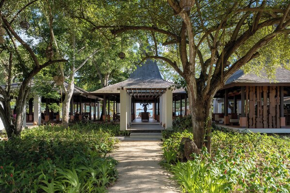 A covered pathway leading to a gazebo-like structure surrounded by lush greenery and trees. - Kuara Lombok - Adults Only Boutique Resort (Mertak)