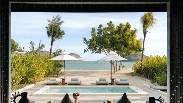 A poolside view with lounge chairs, umbrellas, and a view of the beach and ocean. - Kuara Lombok (Mertak)