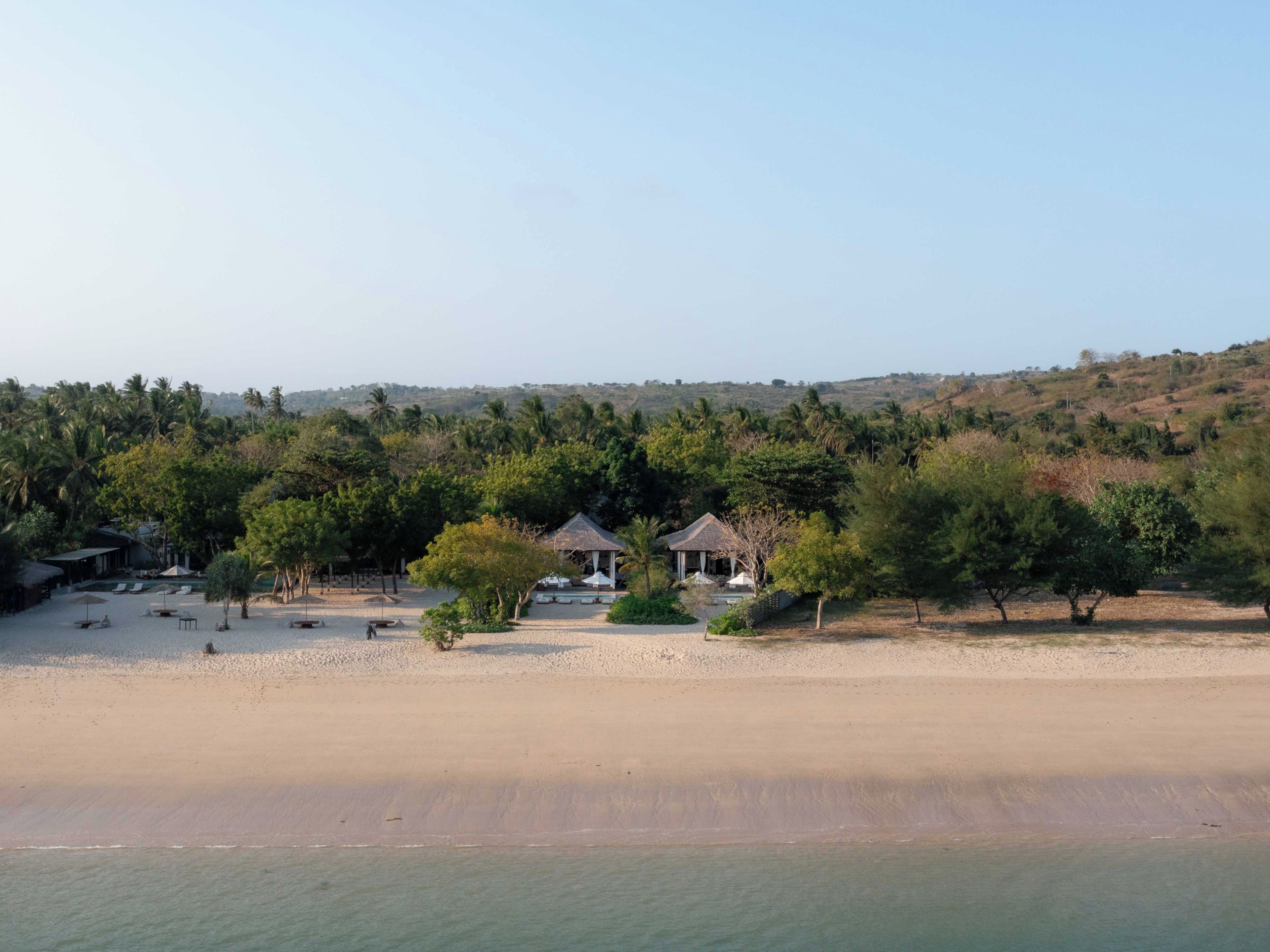 A beachfront property with a sandy beach, several small structures, and dense greenery in the background.