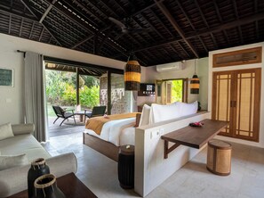 Relax in a comfortable room with a bed, sofa, and dining area, offering a view of lush greenery outside.