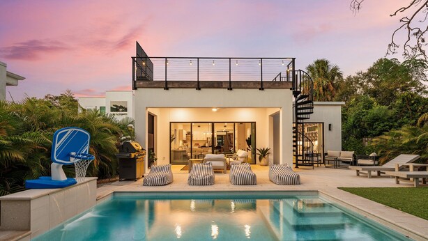A modern house with a pool, outdoor seating, and a staircase leading to a balcony.