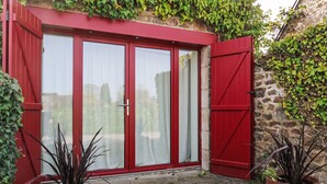 Eine rote Tür mit Glasscheiben, eine Steinsäule und Blumentöpfe.