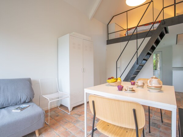 A modern, well-lit room with a white table set for breakfast, a grey sofa, and a staircase leading to an upper level.