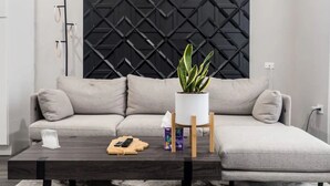 Un salón moderno con un sofá gris, una mesa de centro oscura y un panel de pared geométrico negro.