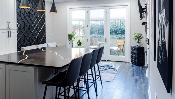 Una cocina moderna con una isla central, lámparas colgantes negras y vistas a un patio exterior.