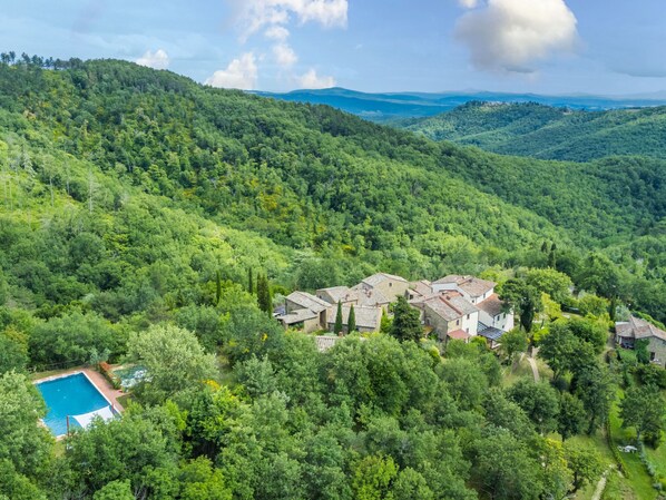 Une villa située sur une colline, comprenant plusieurs bâtiments, une piscine et une végétation luxuriante.
