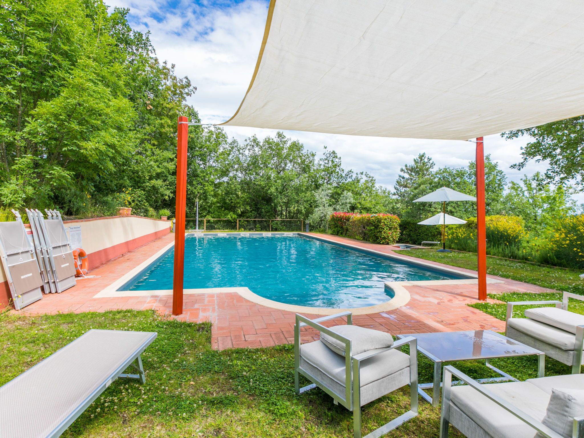 A swimming pool with a sunshade, outdoor seating, and a brick pathway.