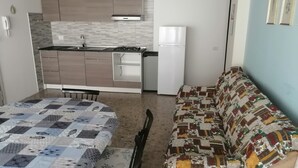 Ein kompakter Wohnbereich mit Küchenzeile, einer Couch, einem Esstisch und einer bettenbezogenen Tagesdecke mit Muster.