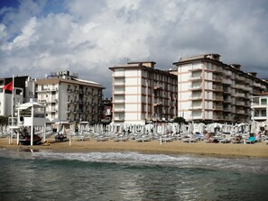 A beachfront hotel with multiple balconies, a rescue service sign, and a row of beach umbrellas.