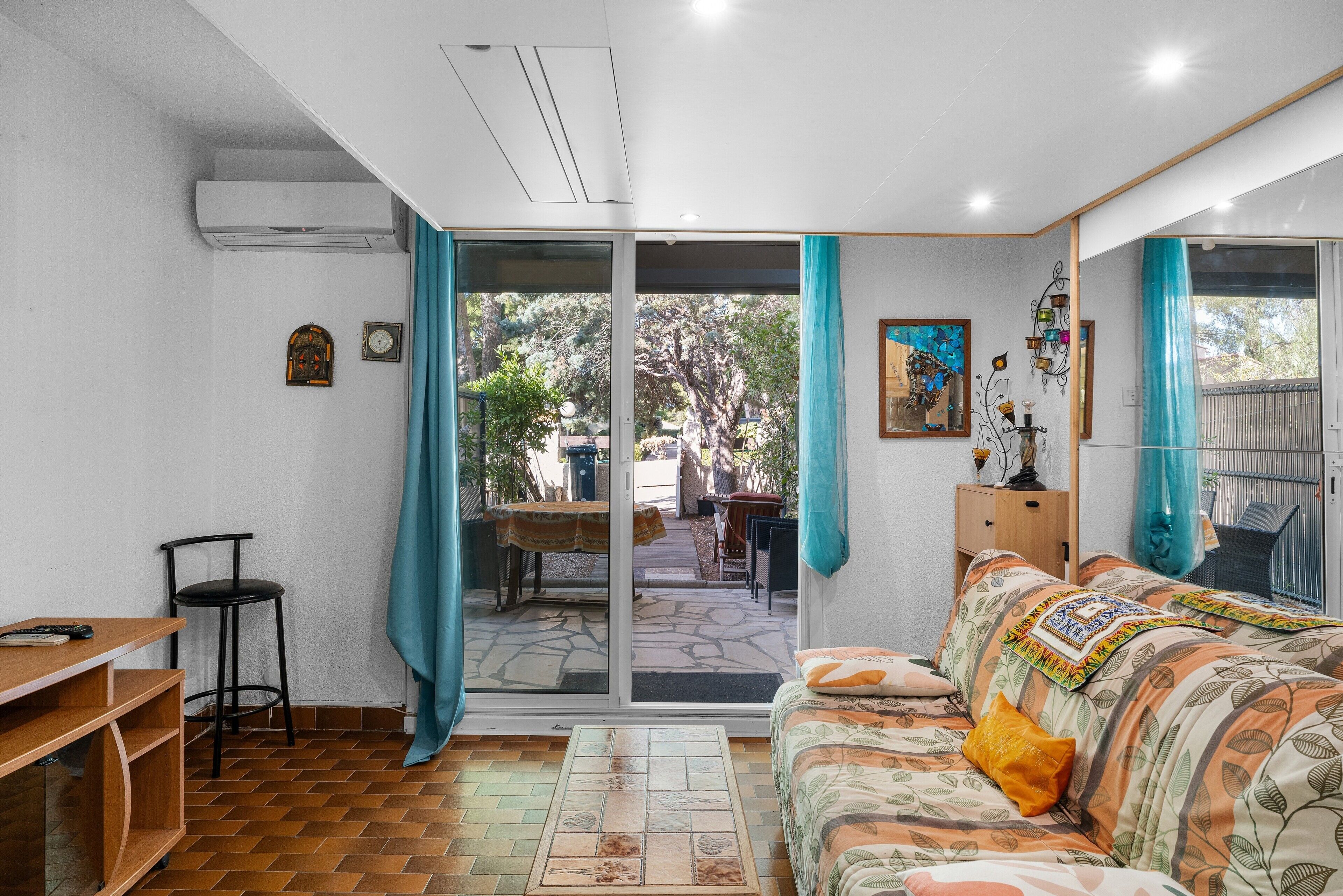 A room with a sofa, a table, a chair, a sliding glass door leading to an outdoor area, and a small clock on the wall.