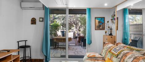 A room with a sofa, a table, a chair, a sliding glass door leading to an outdoor area, and a small clock on the wall.