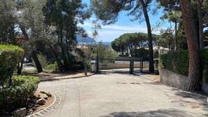 Une allée privée, fermée par un portail, mène à une propriété offrant une vue sur la mer et les arbres environnants.
