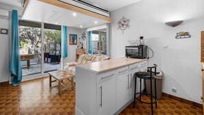 Une cuisine compacte équipée d’un four à micro-ondes, d’un évier et d’un tabouret de bar. Une porte-fenêtre coulissante donne accès à un patio aménagé avec une table et des chaises.