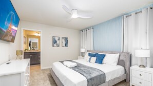 A bedroom with a bed, bedside tables, a ceiling fan, and a view of the bathroom.