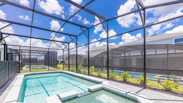 A swimming pool with a hot tub, surrounded by a covered patio area with a view of houses in the background.