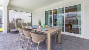 An outdoor patio with a table set for four, surrounded by wicker chairs, and a sliding glass door leading to a balcony.