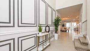 A modern hallway with a marble console table, potted plants, and a staircase leading to another level.