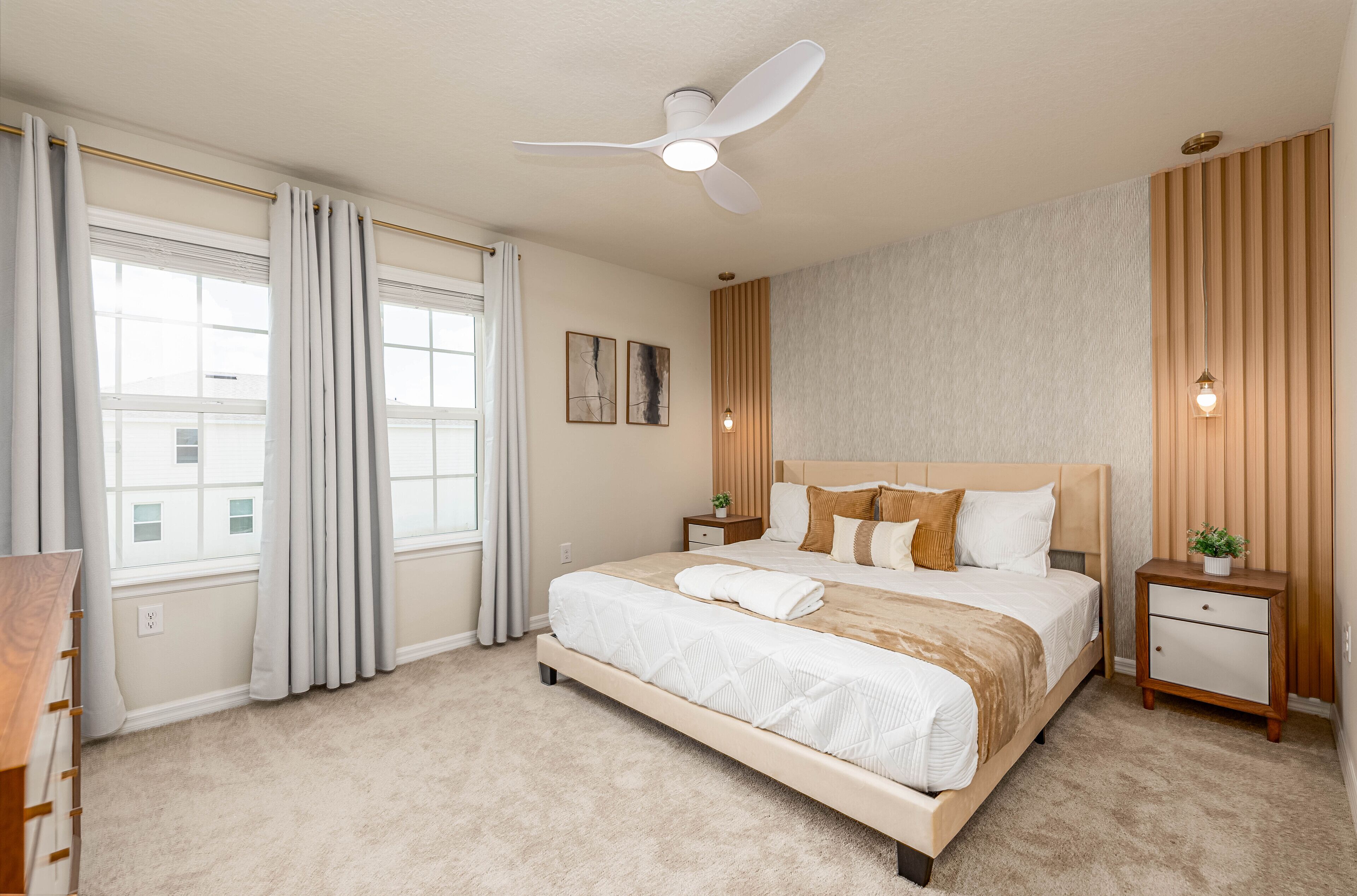 A modern bedroom with a large bed, a ceiling fan, bedside tables, and a window with curtains.
