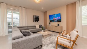A modern living room with a grey sectional sofa, a wooden coffee table, a TV mounted on the wall, and a wooden chair.