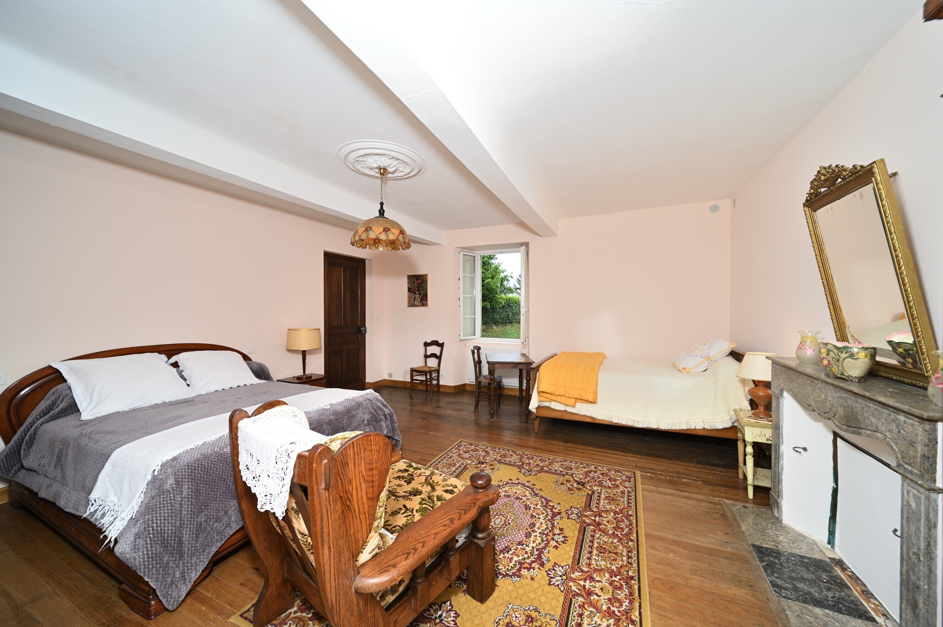 A bedroom with a bed, a chair, a desk, a dresser, a mirror, and a window.