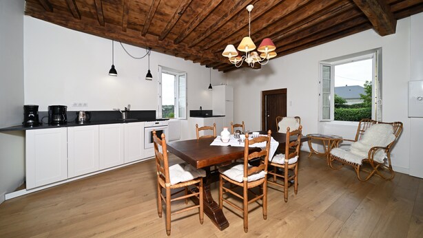 A kitchen with white cabinets, a wooden dining table, and chairs, a hanging light fixture, and a view through a window. - Holiday Home 'La Maison Bayle' with Mountain View, Private Garden & Wi-Fi (Mauvezin)